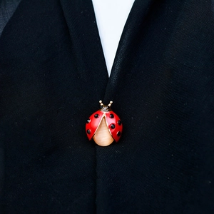 Miniature ladybug brooch with red enamel, golden base and cat eye stone on a black suit