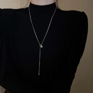 Close-up of silver Y-shaped necklace with geometric zircon pendant on black sweater
