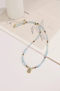 Detail of beaded gemstone necklace with blue stones and a vintage gold relief pendant