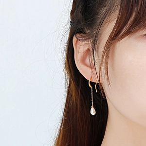 Elegant gold drop earrings with a white teardrop pearl on model against blue backdrop