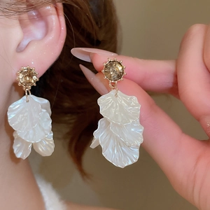 Close-up of golden petal tassel earrings with brown gemstone and white translucent petals