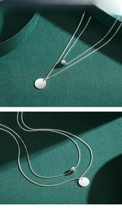 Detail of 925 sterling silver double-layer necklace with ball and disc charms on green background