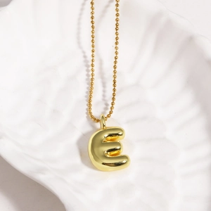 Macro shot of gold bubble letter E pendant on a delicate chain in a white shell tray
