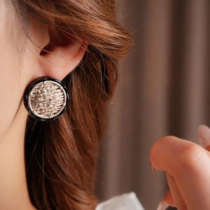 Detail of round gold and black enamel earrings worn on a model with soft lighting