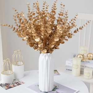 Golden artificial eucalyptus stems in a white geometric ceramic vase for home decor