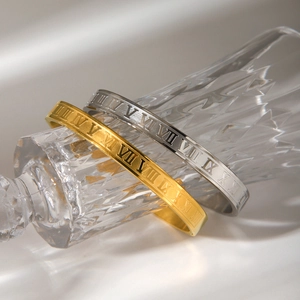 Close-up of gold and silver stainless steel bangles with Roman numeral engravings on glass