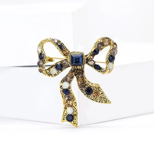 Vintage gold bow brooch with blue crystals and rhinestones on a white background