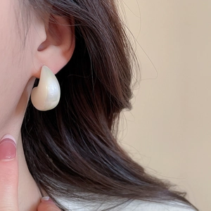 Detail of drop-shaped acrylic earring with creamy pearl finish worn on an ear