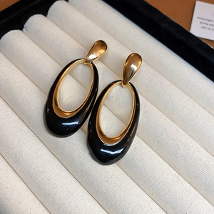 Close-up of vintage black enamel and gold oval drop earrings on beige velvet jewelry tray