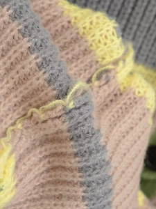 Close-up of colorful striped knit texture in grey pink and yellow thick cardigan