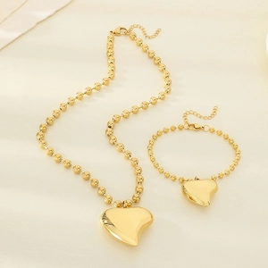 Detail of gold beaded necklace and bracelet set with 3D heart charms on beige fabric