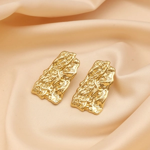 Detail of 18K gold plated earrings featuring a wrinkled texture on beige silk fabric