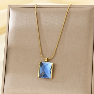 Detail view of rectangular blue gemstone pendant on a gold snake chain necklace