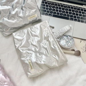 Quilted bow texture cosmetic bags in silver and pearl white shown with accessories