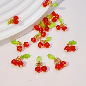 Close-up of red cherry fruit charms with green leaves and gold rings for DIY jewelry