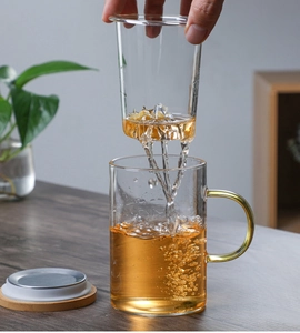 Detail of lifting glass infuser with tea flowing into the cup and wooden lid
