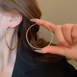 Close-up of large gold geometric hoop earrings worn to show minimalist metal texture