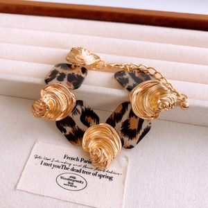 Detail of gold metal bracelet with leopard print acrylic blocks and swirl design links