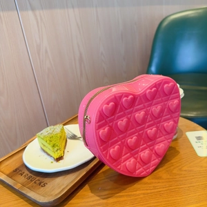 Close-up of pink heart-shaped bag with quilted texture and gold zipper on a table