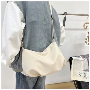 Minimalist beige dumpling bag shown on shoulder in a stylish studio setting