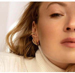 Close-up of golden C-shaped twisted rope earrings and ear cuff on model with metallic glow