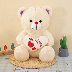 Beige teddy bear with purple ears holding a white Love heart plush on a straw mat