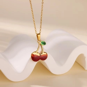 Close-up of a gold chain necklace with red cherry pendants and a green leaf detail