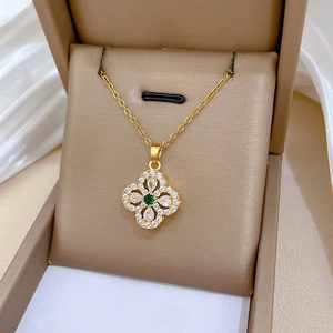 Close-up of gold clover necklace with zircon pavé and green gem in a jewelry box