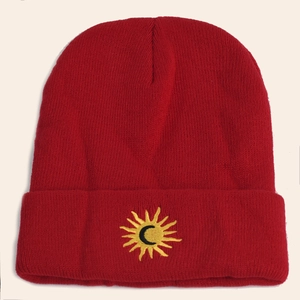 Detailed view of the red knitted beanie featuring a sun and moon embroidery logo