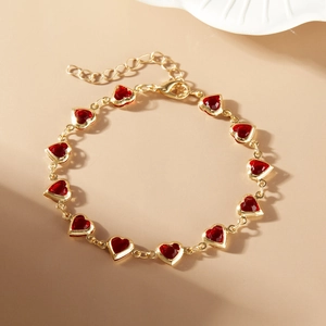 Macro shot of gold bracelet with red heart gems and lobster clasp detail