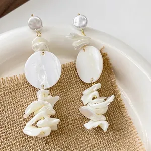 Close-up of white Baroque pearl tassel earrings with gold-tone links on a rustic setting