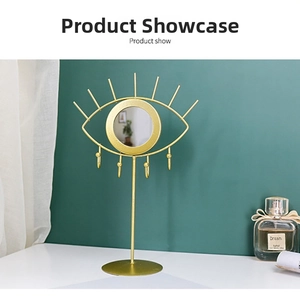 Golden eye-shaped jewelry stand with central round mirror and four hanging hooks