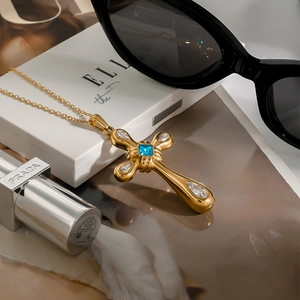 Gold cross necklace with blue gemstone and zircons on jewelry box and magazine