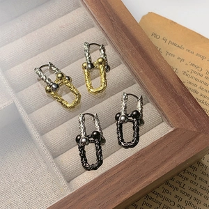 Vintage industrial style U-shaped metal earrings with two-tone finish on a wooden tray