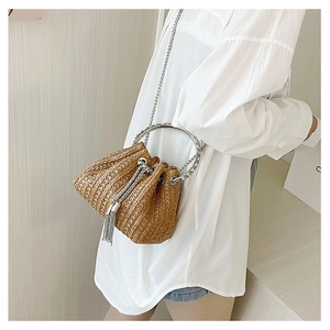 Close-up of brown straw bucket bag featuring silver ring handles and tassel details