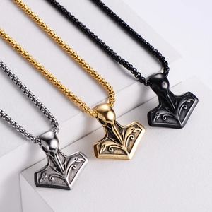 Three Viking Mjölnir raven head pendants in silver, gold, and black on stone steps
