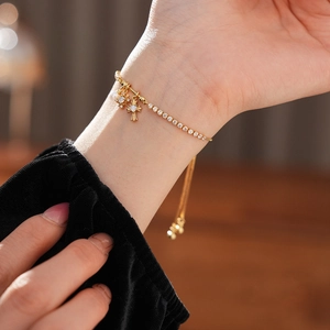 Close-up of a gold cross and zircon star pendant bracelet worn on a female wrist