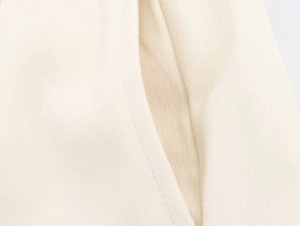 Dettaglio macro delle cuciture su pantaloni larghi beige che mostrano la trama del cotone