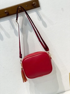 Rote Kameratasche mit Narbenleder, geometrischem Schultergurt und buntem Quastenanhänger