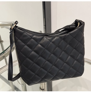 Close-up of black quilted shoulder bag featuring gold metal rings and zipper detail