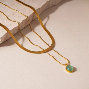 Détail de la chaîne serpent dorée et collier perlé avec pendentif ovale en œil de chat