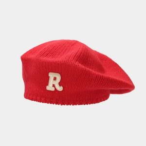 Detail of red knitted beret with white R-letter embroidery and soft wool texture