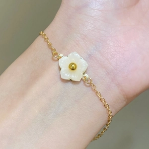 Close-up of adjustable gold chain bracelet featuring a white five-petal flower on wrist