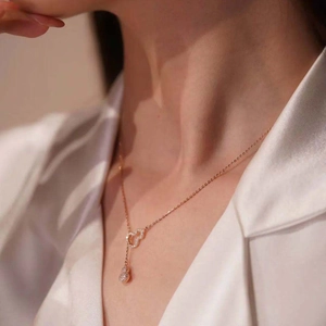 Close-up of a gold titanium necklace with heart and gourd pendants on a silk shirt