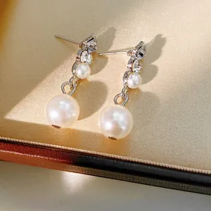 Elegant pearl drop earrings with diamond-studded silver base on a satin jewelry box lining