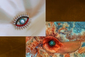Artistic detail of gold evil eye brooch with freshwater pearl and red enamel inlay