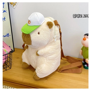 Cute capybara plush backpack with a green baseball cap on a cozy wooden table setup