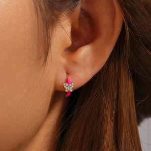 Close-up of butterfly hoop earring in gold with pink enamel and sparkling zircons