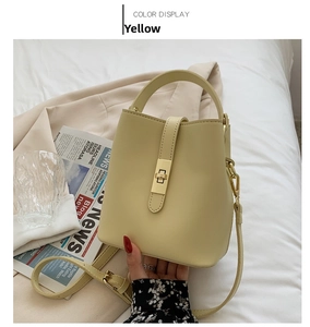 Close-up of yellow bucket handbag with gold buckle and strap on white fabric