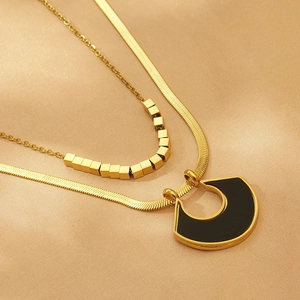 Detail of layered gold snake chain and beaded necklace with black U-shaped pendant
